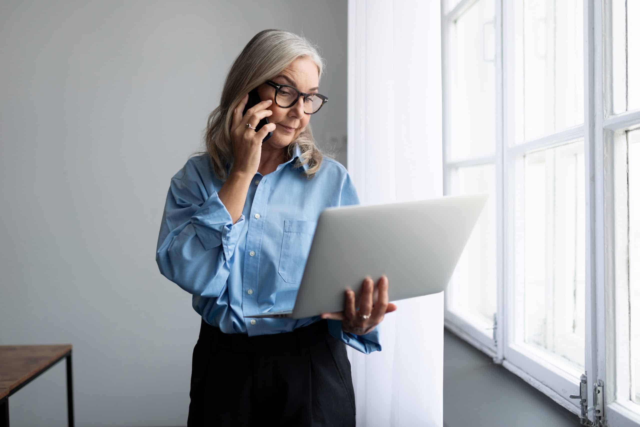 adult fifty-year-old female business consultant speaks on a mobile phone with a laptop in her hands